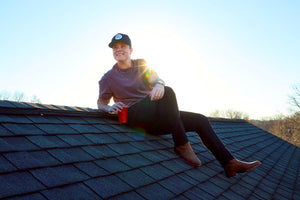 Lily Rose sitting on a rooftop, smiling past the camera and holding a red solo cup